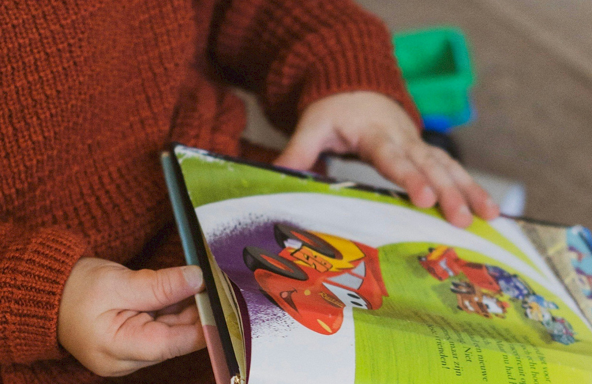 Ein Kind im Kleinkind-Alter sitzt auf dem Boden und sieht sich ein Bilderbuch an.